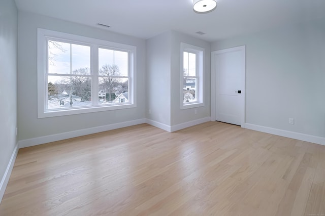 unfurnished room with light wood-style floors, visible vents, and baseboards