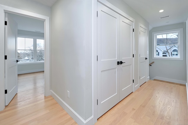 corridor featuring light wood-style floors, visible vents, baseboards, and a wealth of natural light