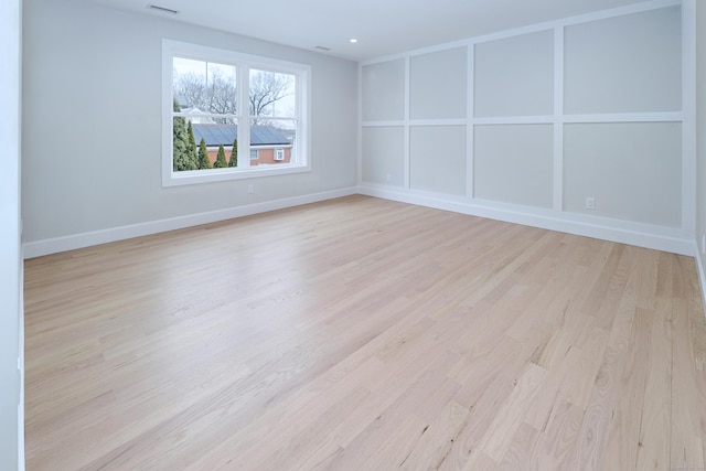 unfurnished room with light wood finished floors, visible vents, baseboards, and a decorative wall