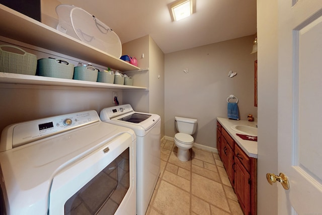 clothes washing area with stone tile flooring, a sink, laundry area, independent washer and dryer, and baseboards