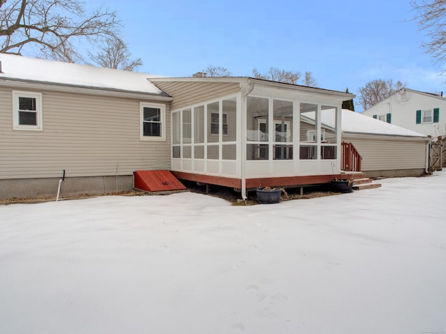 snow covered back of property with a sunroom