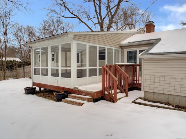 snow covered back of property with a chimney, fence, and a sunroom