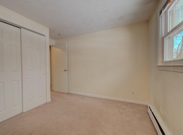 unfurnished bedroom featuring a baseboard heating unit, a closet, baseboards, and light colored carpet