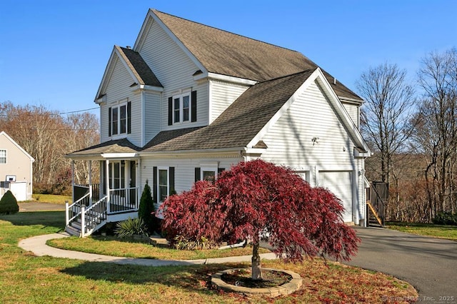 view of side of property featuring a garage, covered porch, aphalt driveway, and roof with shingles