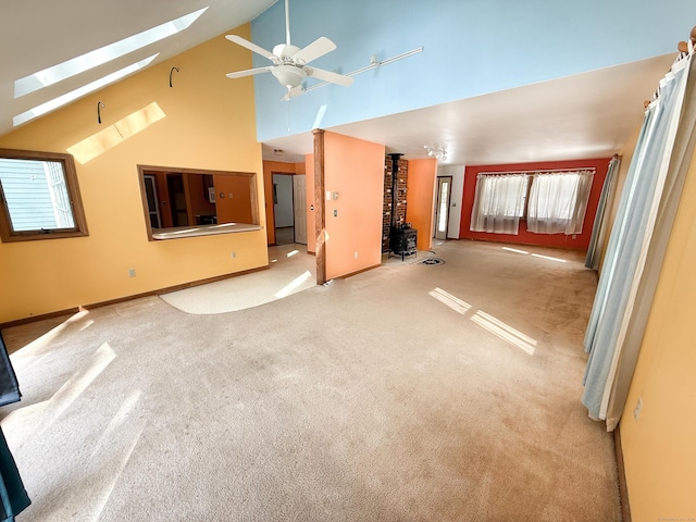 unfurnished living room with ceiling fan, a skylight, high vaulted ceiling, and light carpet