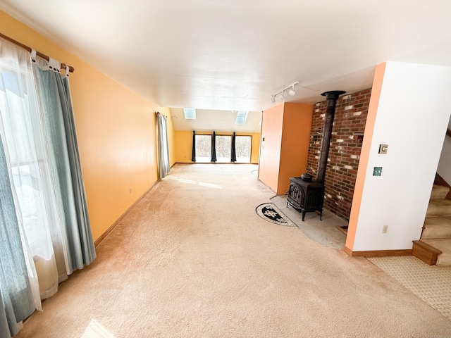 unfurnished room with light carpet, stairway, track lighting, and a wood stove