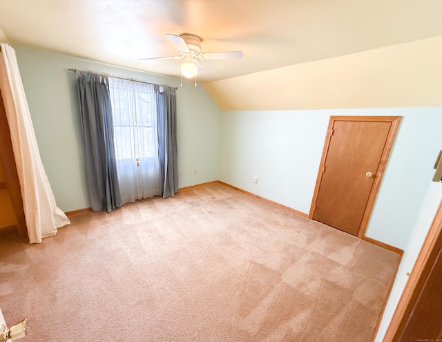 interior space with light colored carpet, ceiling fan, baseboards, and vaulted ceiling