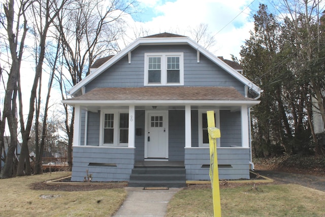 bungalow featuring covered porch, a shingled roof, and a front yard