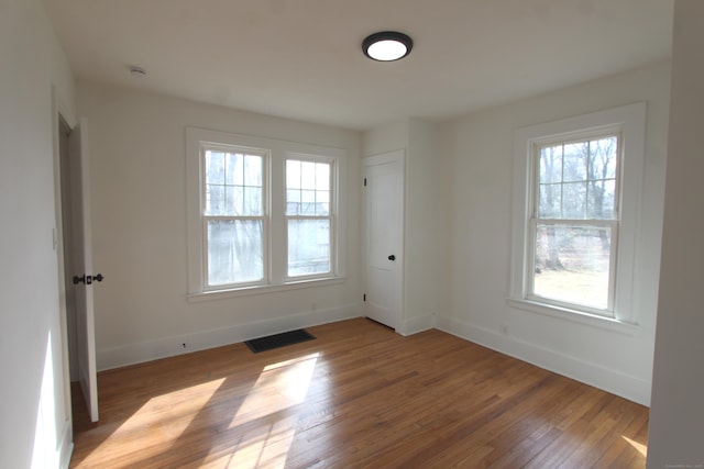 empty room with wood-type flooring, visible vents, plenty of natural light, and baseboards