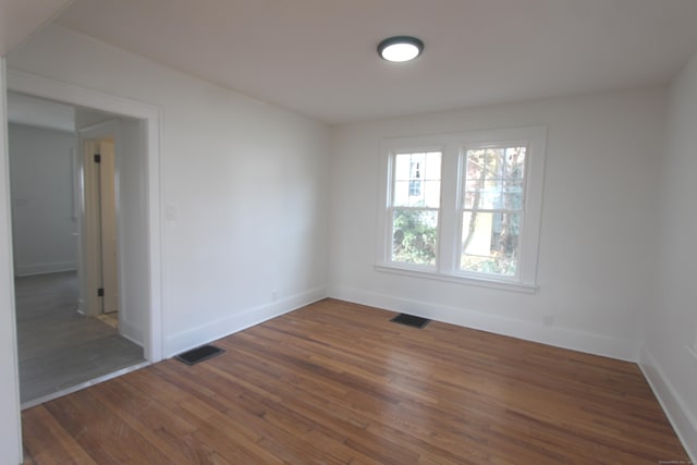 unfurnished room featuring wood finished floors, visible vents, and baseboards