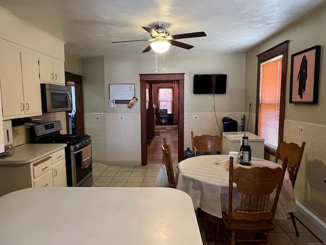 dining area with a ceiling fan, a wainscoted wall, tile walls, and light tile patterned floors