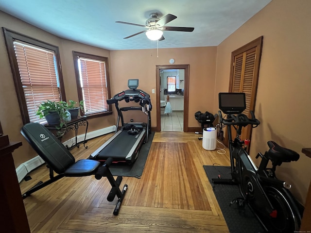 exercise room featuring a ceiling fan, baseboard heating, baseboards, and wood finished floors