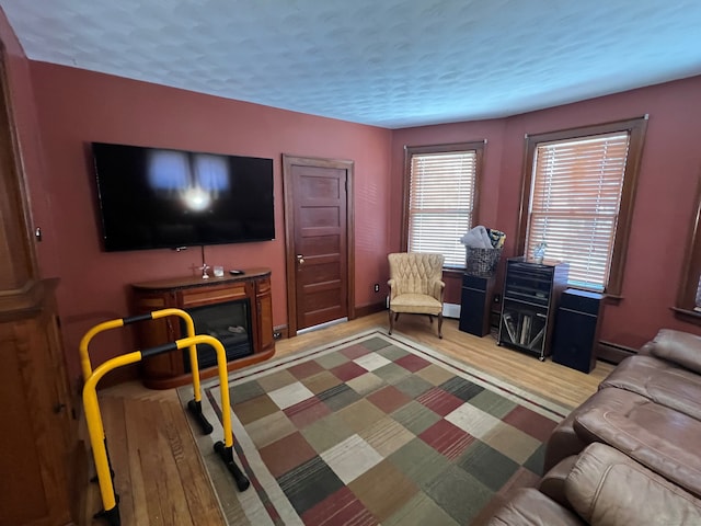 living room featuring a baseboard heating unit, light wood-type flooring, a fireplace, and a textured ceiling