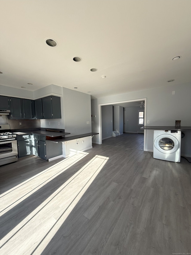 kitchen featuring under cabinet range hood, dark wood-style flooring, stainless steel range with gas cooktop, washer / clothes dryer, and dark countertops