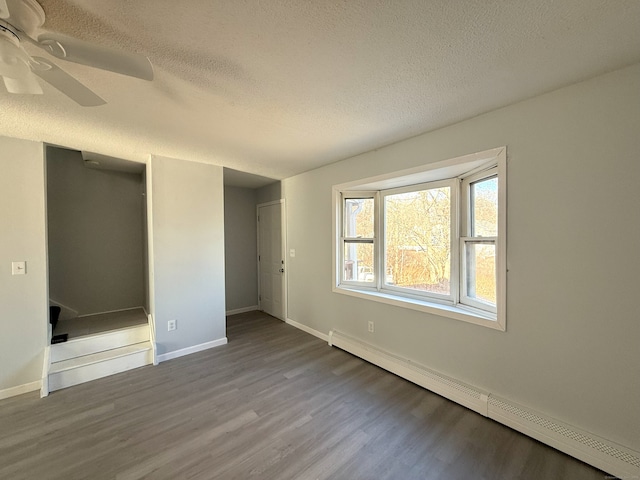 unfurnished bedroom with baseboards, ceiling fan, wood finished floors, a textured ceiling, and a baseboard heating unit