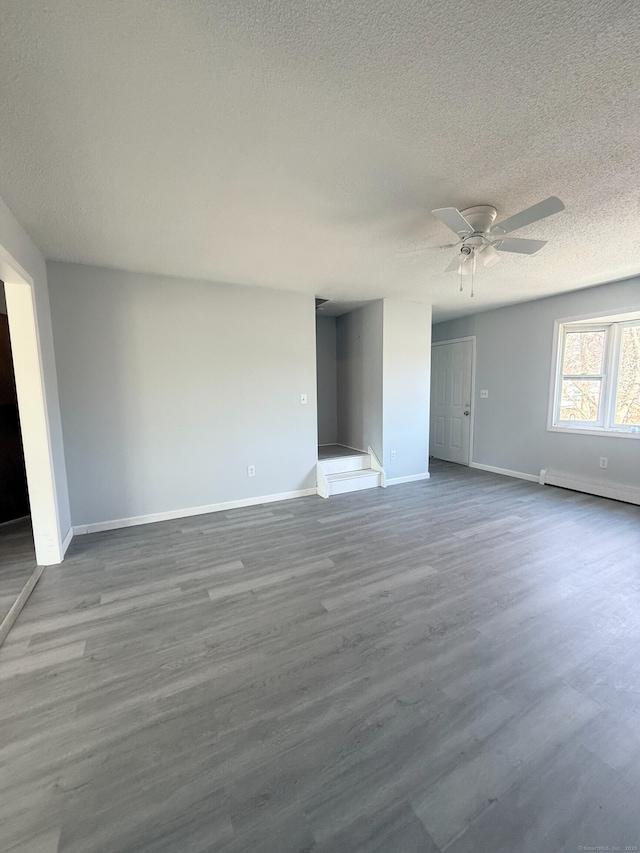 interior space with baseboard heating, ceiling fan, a textured ceiling, wood finished floors, and baseboards