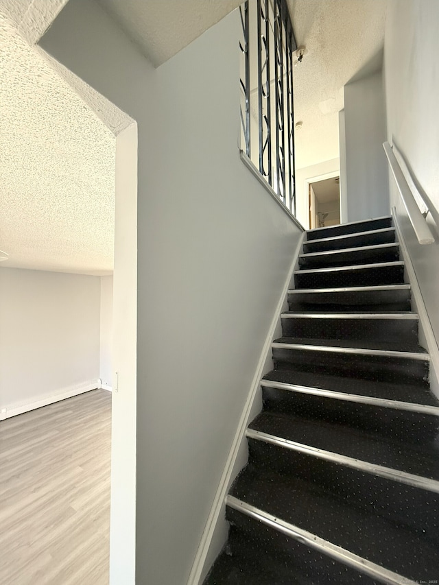 stairway with baseboards, baseboard heating, a textured ceiling, and wood finished floors