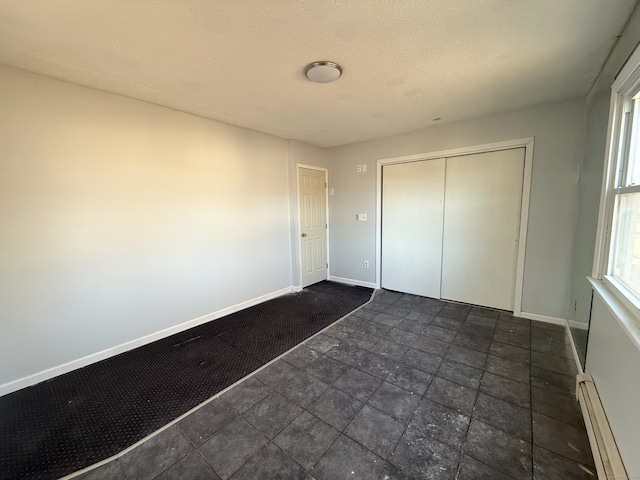 unfurnished bedroom with a closet, baseboards, a textured ceiling, and baseboard heating