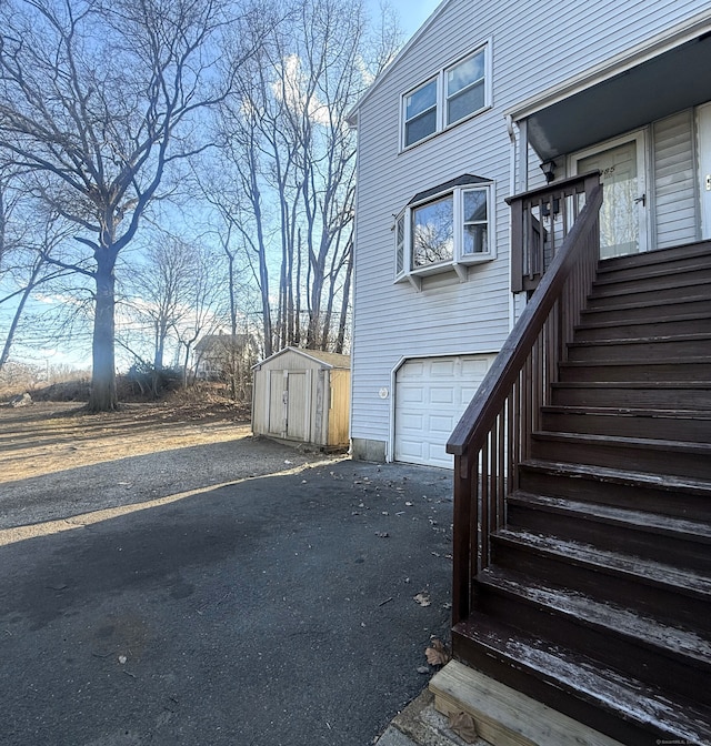 view of property exterior with aphalt driveway, an outbuilding, a storage unit, stairway, and a garage