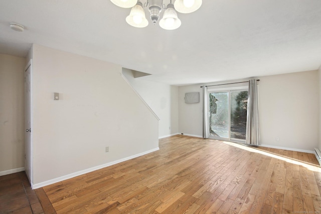 unfurnished living room with a notable chandelier, baseboards, and light wood-style floors