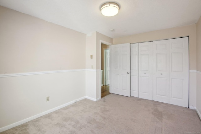 unfurnished bedroom with a closet, baseboards, and light colored carpet