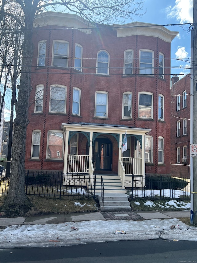 view of front facade with covered porch, brick siding, and fence