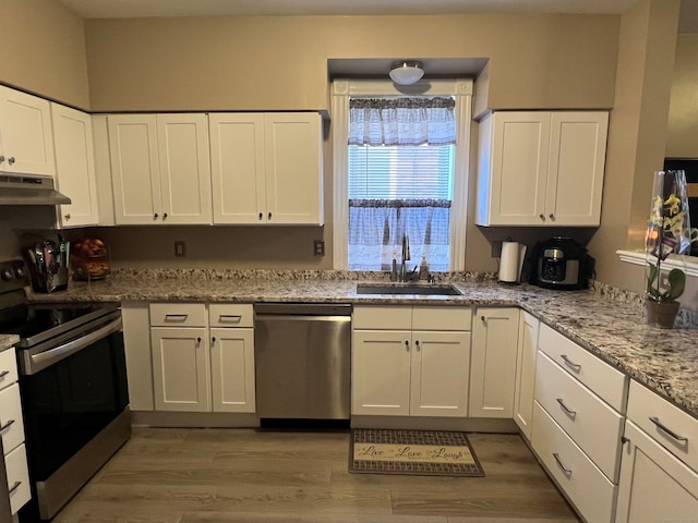 kitchen with under cabinet range hood, a sink, white cabinetry, light wood-style floors, and appliances with stainless steel finishes