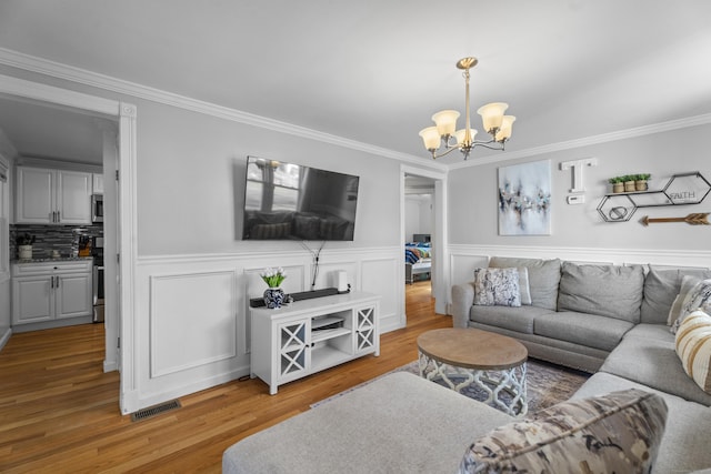 living area with visible vents, an inviting chandelier, wood finished floors, and crown molding