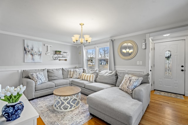 living room featuring light wood-style flooring, a notable chandelier, ornamental molding, and wainscoting