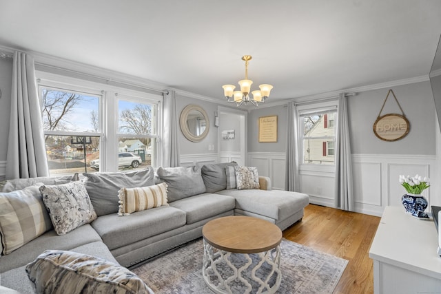 living area with a notable chandelier, wainscoting, crown molding, and light wood finished floors