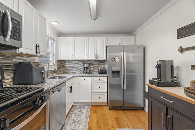 kitchen with light wood finished floors, white cabinetry, stainless steel appliances, and a sink