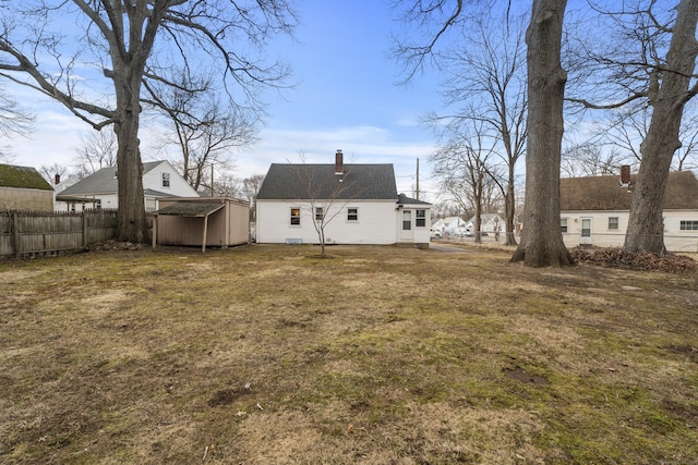 back of property with an outbuilding, fence, a yard, a chimney, and a storage unit