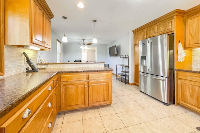 kitchen with light tile patterned floors, a peninsula, stainless steel refrigerator with ice dispenser, brown cabinetry, and a ceiling fan