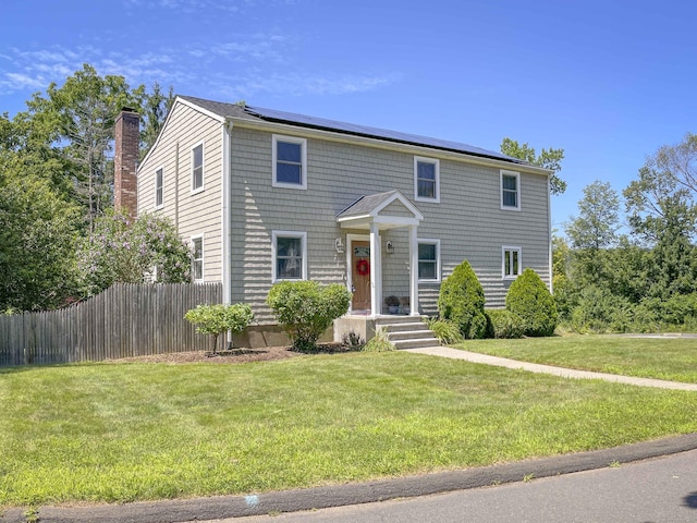 view of front of property with a front lawn, fence, roof mounted solar panels, and a chimney