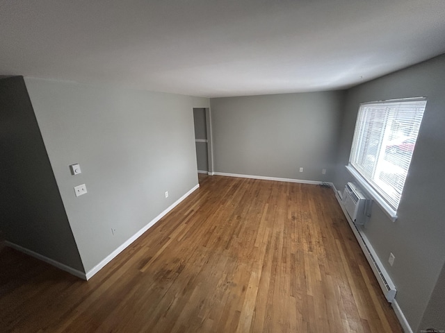 spare room featuring a baseboard heating unit, a wall mounted air conditioner, wood finished floors, and baseboards