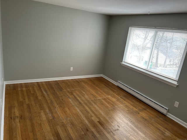 empty room with a baseboard heating unit, wood-type flooring, and baseboards