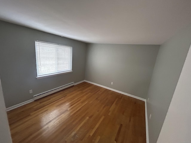 spare room featuring a baseboard heating unit, wood finished floors, and baseboards