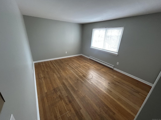 empty room with a baseboard heating unit, baseboards, and dark wood-style floors