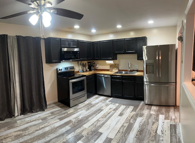 kitchen with light wood-style flooring, appliances with stainless steel finishes, dark cabinets, light countertops, and a sink