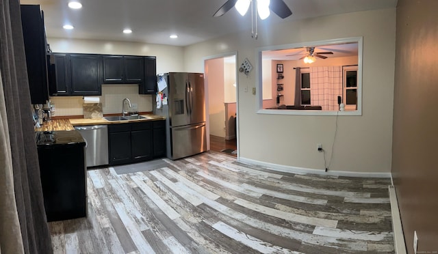 kitchen with stainless steel appliances, backsplash, a sink, light wood-type flooring, and dark cabinetry