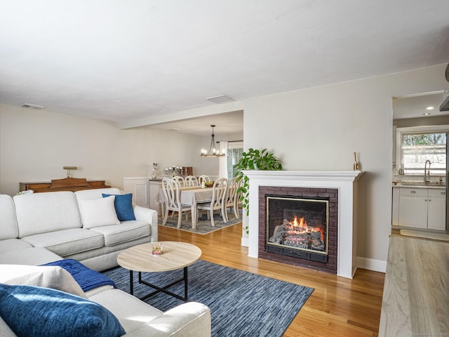 living room with light wood-type flooring, a brick fireplace, visible vents, and a chandelier