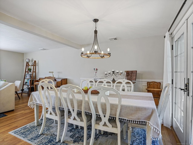 dining area with a chandelier, beam ceiling, wood finished floors, and visible vents