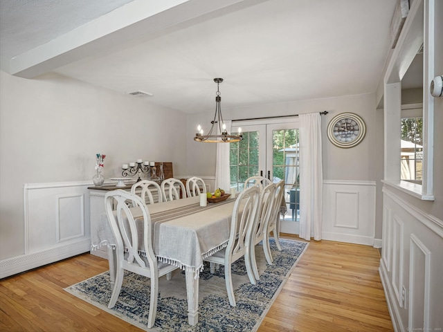 dining area with a wainscoted wall, a notable chandelier, visible vents, a decorative wall, and light wood-style floors