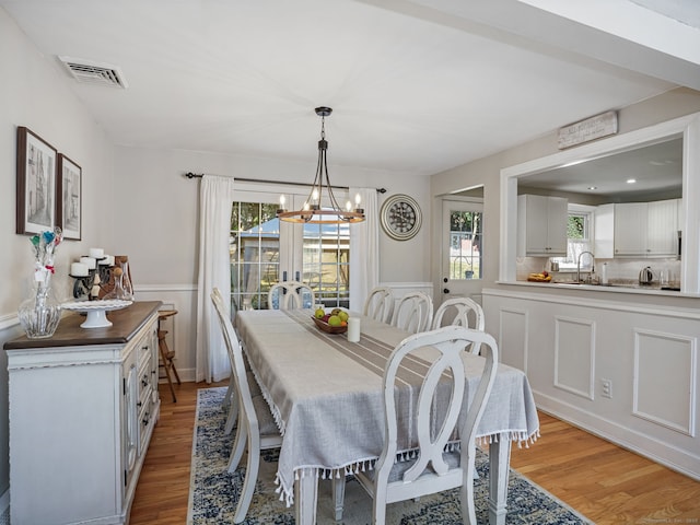 dining room with light wood-type flooring, a wainscoted wall, visible vents, and a chandelier