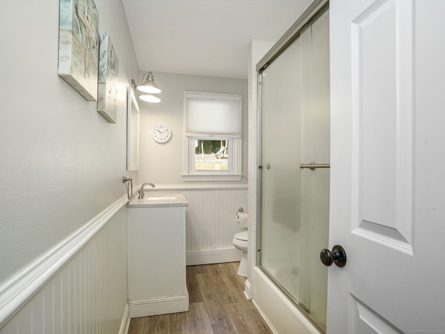 bathroom featuring wainscoting, toilet, enclosed tub / shower combo, wood finished floors, and vanity