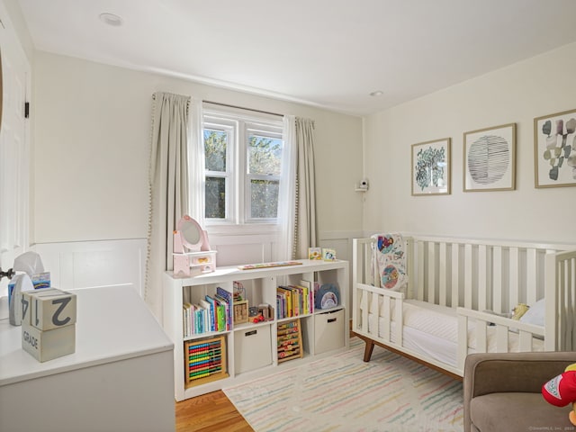 bedroom featuring a wainscoted wall, a decorative wall, a crib, and wood finished floors