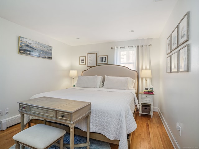 bedroom with light wood-type flooring, baseboards, and a baseboard heating unit