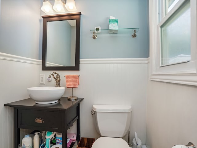 half bath with wainscoting, vanity, and toilet