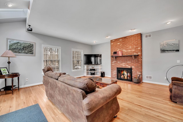 living area featuring visible vents, a brick fireplace, light wood-type flooring, and baseboards