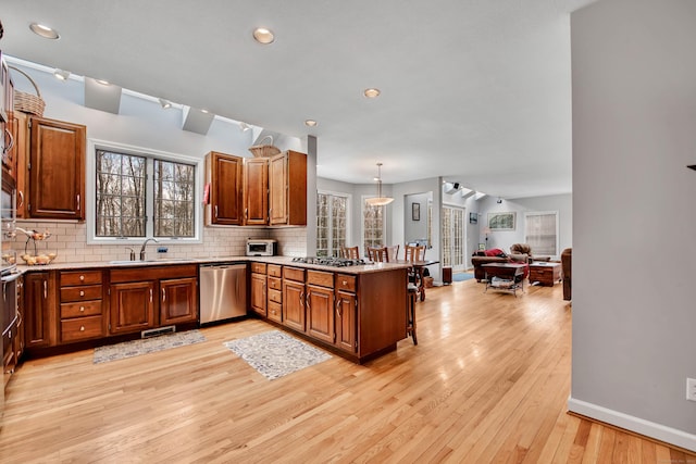 kitchen with backsplash, dishwasher, a peninsula, light wood-style floors, and a sink